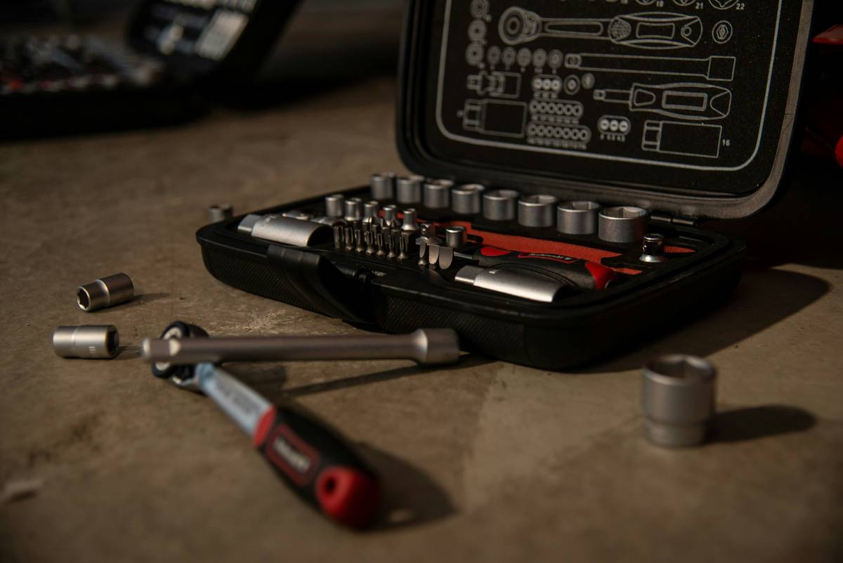 essential tools for home repairs laid out on a workbench including hammer, adjustable wrench, screwdrivers, tape measure, level, utility knife, and cordless drill