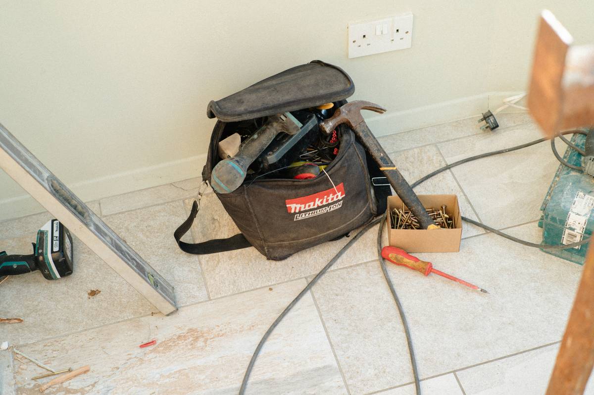 home maintenance repair tool that i essentials laid out on workbench including multimeter, cordless drill, and pipe wrench